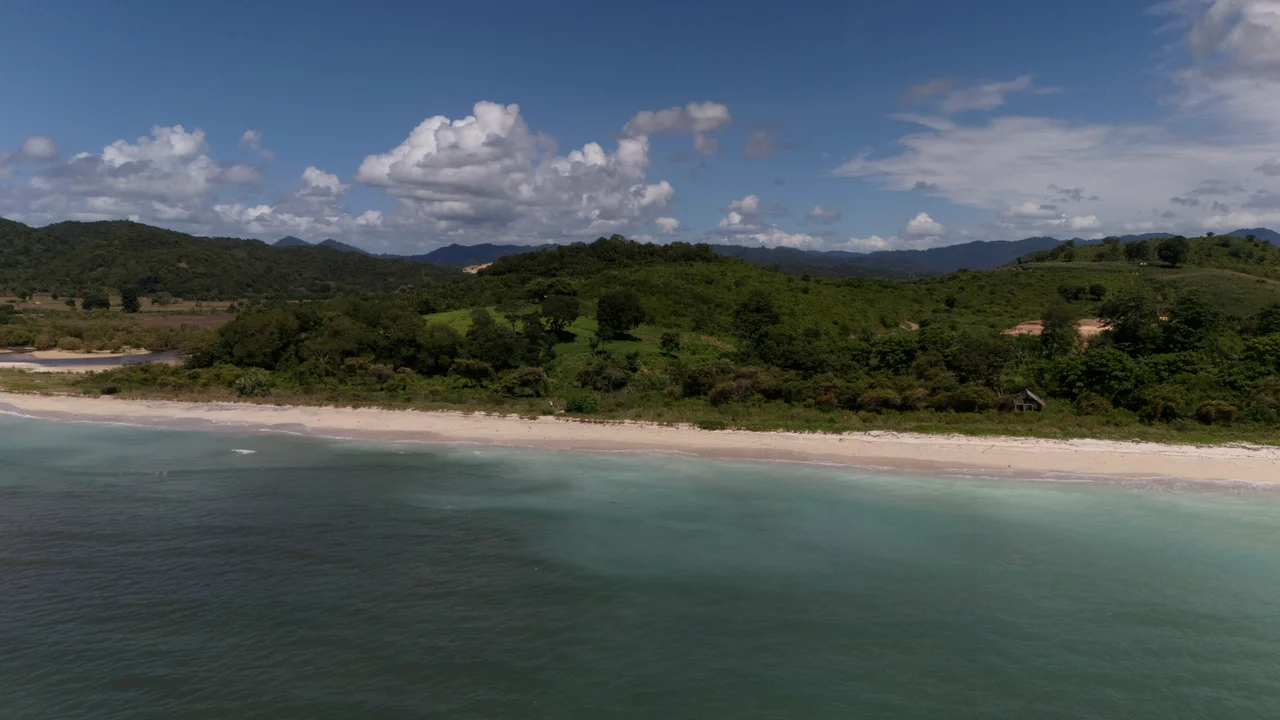 Aerial drone view of the land plot on a green hilltop with white-sand beach and turquoise ocean, West Sumbawa
