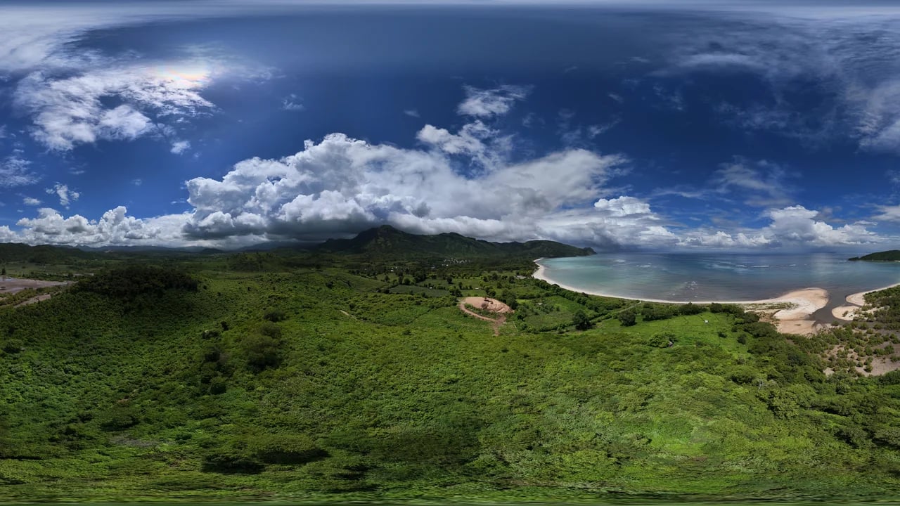 Wide panoramic aerial view of the bay, white-sand beach, surrounding jungle and dramatic cloudy sky from above the hilltop plot