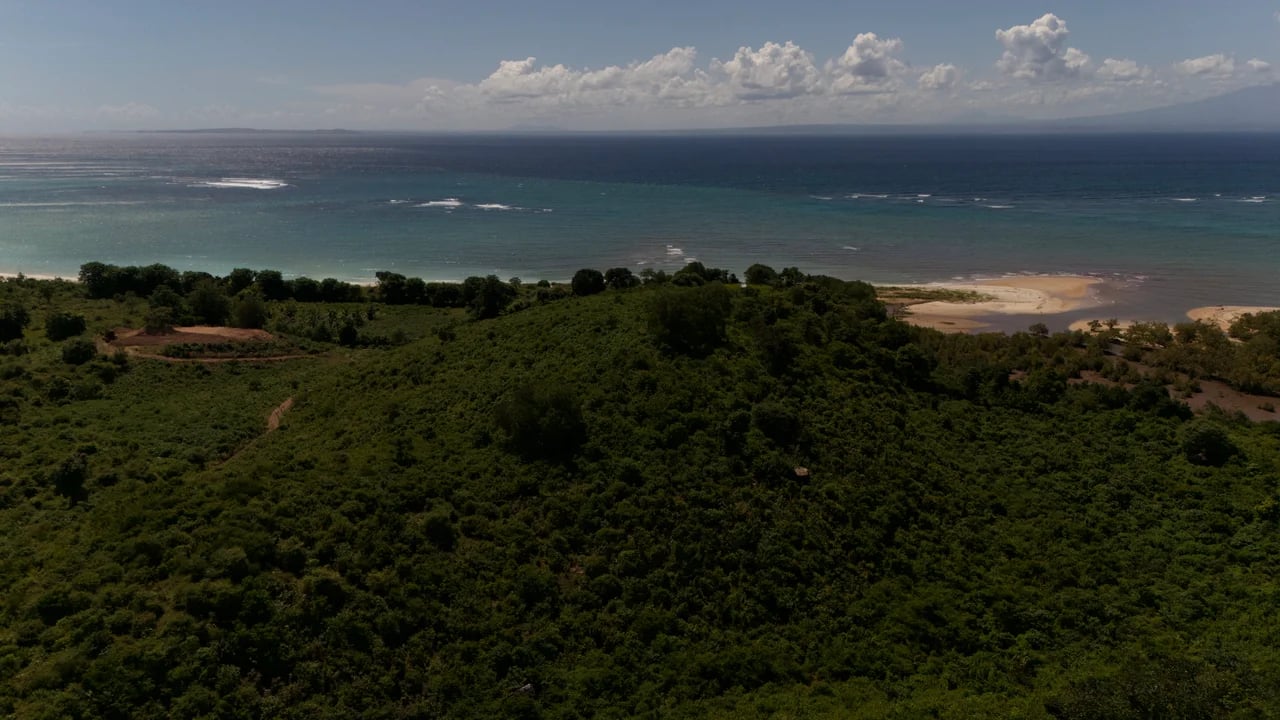 Aerial view looking seaward — surf breaks visible on the horizon beyond the hilltop land plot